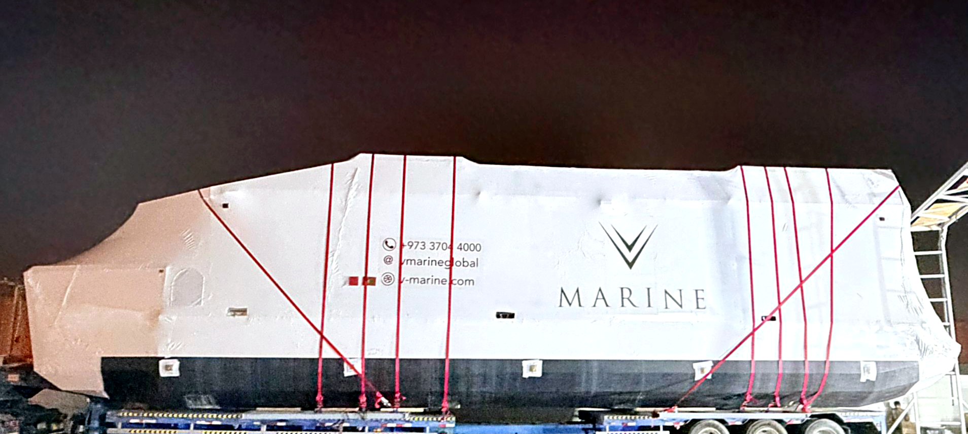 A wrapped, V-Marine branded hull secured on a low-bed trailer for worldwide shipping